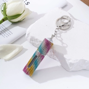 Close-up of rainbow rhinestone perfume bottle keychain on a white decorative stone