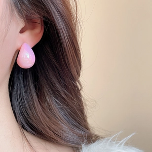 Close-up of a pink pearlescent waterdrop earring worn by a model with soft lighting