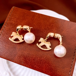 Detail view of vintage golden rocking horse earrings with large white pearls on leather