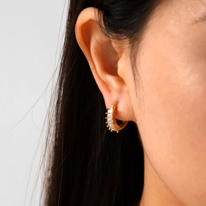 Detail of gold-plated hoop earring with baguette-cut cubic zirconia on a model's ear