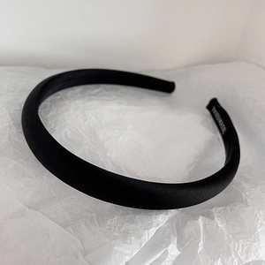 Detailed view of black satin headband on white paper with handmade label tag