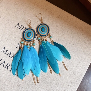 Macro detail of bohemian blue feather earrings with gold chains and enamel beads