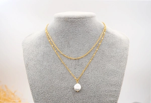 Detail of layered gold titanium necklace featuring a white pearl pendant on a velvet neck bust