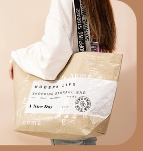Detail of a large beige woven tote bag with white lettering worn by a model
