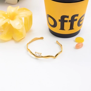 Détail d'un bracelet jonc doré ondulé en acier inoxydable avec un zircon carré