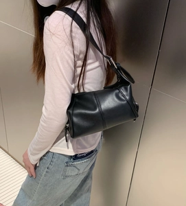Side view of black leather underarm bag with silver hardware on model against metallic wall