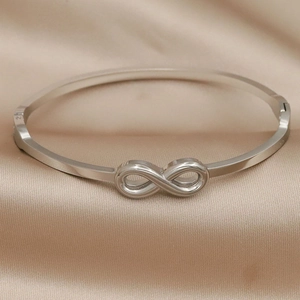 Silver infinity symbol bangle in polished stainless steel on champagne silk background