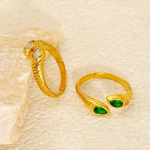 Golden textured band rings featuring pear-cut white and emerald green stones in warm lighting
