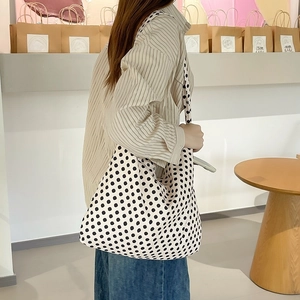 Detail view of cream canvas tote bag with black polka dot pattern worn on shoulder