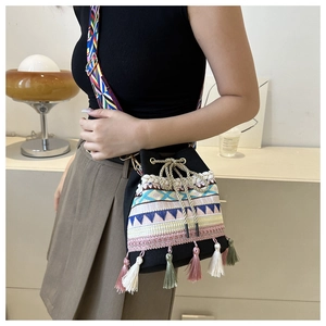 Close-up of ethnic bucket bag with colorful embroidery and tassels on woven strap
