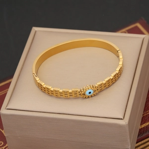 Detail of gold evil eye bracelet with hollow geometric mesh on a beige jewelry box