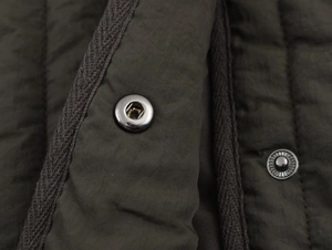 Gros plan d'une veste matelassée olive montrant les coutures et le bouton-pression en métal