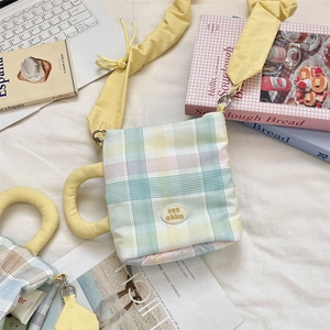 Close-up of a coffee cup shaped plaid bag with ruffled strap and brand badge