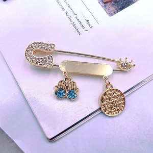 Macro shot of gold-toned safety pin brooch with Hamsa charms and blue rhinestones
