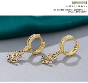 Close-up of golden anchor earrings with colorful crystals on a silk backdrop