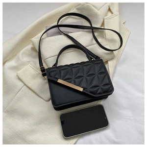Top view of black quilted crossbody bag with gold metal trim on a white blazer background