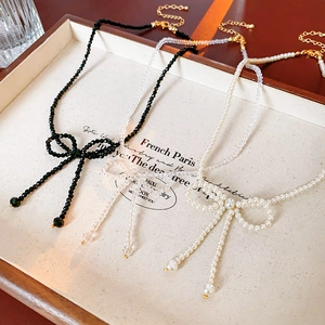 Detailed shot of bow necklaces with black, transparent, and white pearl beads on a tray