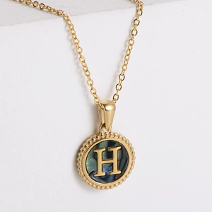 Close-up of golden round pendant with embossed letter H and iridescent shell inlay detail