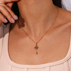 Detail of a gold key necklace with green gemstone inlay worn on a neck model