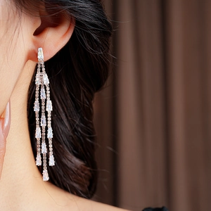 Macro shot of long rose gold tassel earrings with sparkling crystals worn by a model
