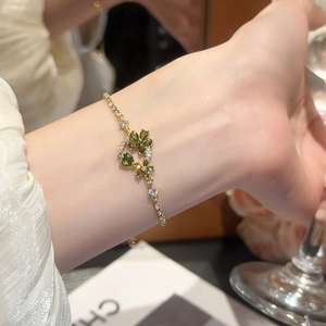 Detail of 18k gold plated bracelet with green heart zirconia flower on a female wrist