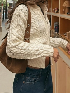 Detail of white cable knit cardigan with zipper paired with blue jeans and brown suede bag
