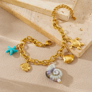 Detail of gold chain bracelet with sea star, fish, snail, and turtle charms on stone background