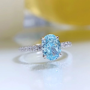 Macro shot of oval light blue zircon ring with silver prong setting and micro-pave band