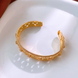 Detail of gold-plated cuff bracelet featuring floral zircon inlay and hollow clover patterns