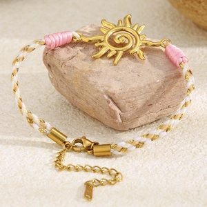 Détail d'un bracelet tissé avec pendentif soleil doré 18K enroulé autour d'une pierre