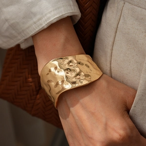 Close-up of golden irregular hammered wide cuff bracelet with a glossy mirror finish