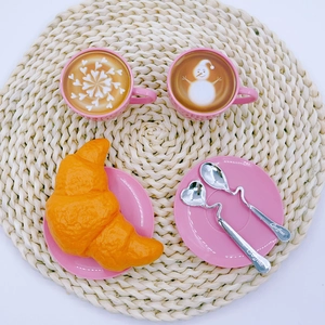 Detailed top view of pink toy coffee cups with spoons and croissant on a woven mat