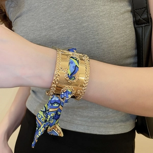 Detailed shot of gold metal cuff bracelet wrapped with blue patterned silk scarf accessory
