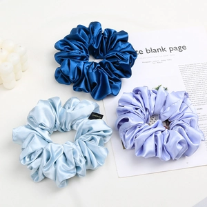 Close-up of three satin scrunchies in blue and purple tones with silk-like glossy finish