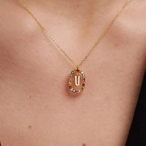 Gold pendant necklace with letter U and colorful zircon stones in oval frame on model