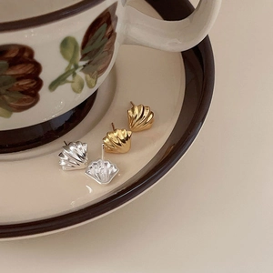 Detailed view of gold and silver shell earrings on a vintage ceramic saucer