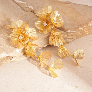 Detailed close-up of golden metal mesh flower earrings with rhinestones on a stone base