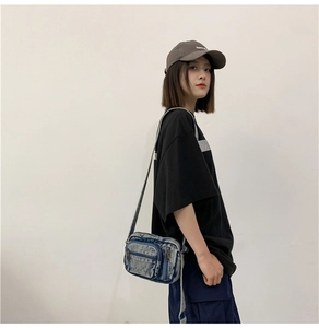 Detail of blue washed denim crossbody bag with multiple zippers and adjustable shoulder strap