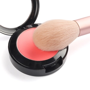 Gros plan sur blush corail en poudrier noir avec un pinceau de maquillage rose doré