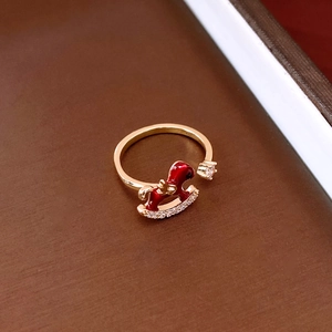 Close-up of golden rocking horse ring with red enamel and sparkling zircon details
