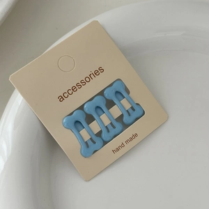 Close-up of three light blue bone-shaped hair clips on white ceramic plate