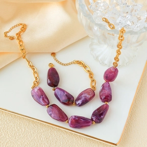 Detail view of gold chain necklace with irregular purple stone beads on white ceramic tray