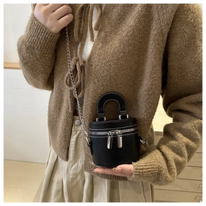 Détail du sac cylindrique noir avec bandoulière chaîne argentée porté par un mannequin