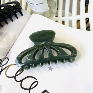 Detail showing deep green hollow flower hair claw clip on white magazine background