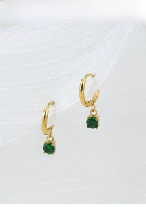 Detail of gold-plated hoop earrings with a green gemstone drop on white fabric