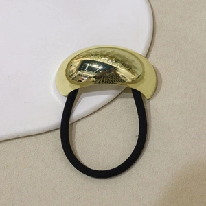 Minimalist U-shaped alloy hair tie in gold finish with black elastic band on beige fabric