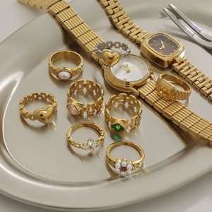 Elegant gold-plated watch and ring set with emerald and pearl accents on a metal tray