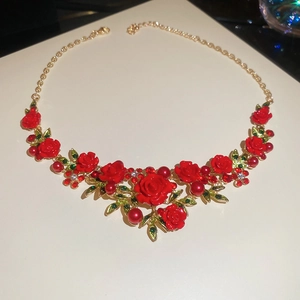 Detail of gold chain necklace with red roses, green leaves, pearls and crystals