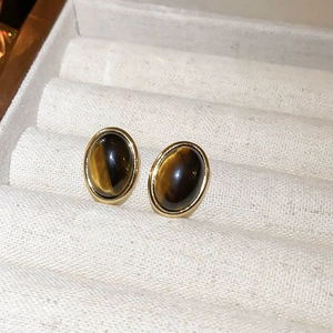 Close-up of vintage oval tiger eye stones set in golden geometric earrings on jewelry tray