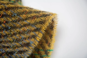 Macro view of gradient tweed shawl fabric with yellow herringbone weave and fringe edges